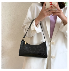 Detail of black faux crocodile leather shoulder bag with golden hardware accents