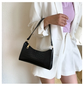 Close-up of black crocodile pattern baguette bag with gold zipper on white blazer