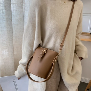 Brown leather bucket bag with adjustable strap worn as a stylish crossbody on a beige sweater