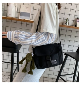 Close-up of black canvas messenger bag with fashion patch and green frog plush pendant