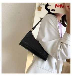 Close-up of black crocodile embossed shoulder bag with gold hardware worn by model