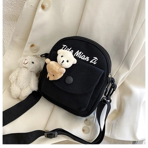 Detail of black canvas crossbody bag featuring cute bear dolls and embroidery on beige suit