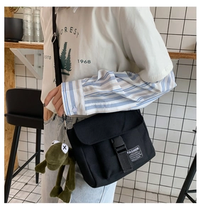 Detail of black canvas messenger bag with adjustable buckle and green frog plush charm