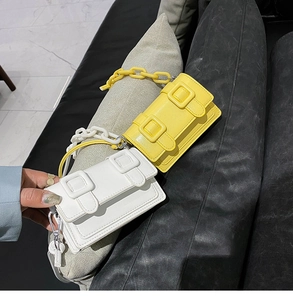 Detail van gele en witte mini crossbodytassen met sierkettingen en glanzende afwerking