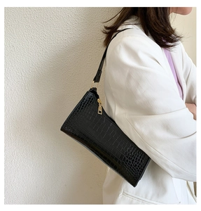 Detail of black crocodile texture baguette bag with golden zipper and metal hardware