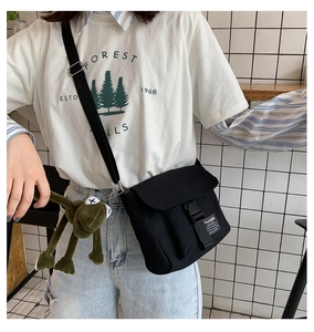 Detail of black canvas messenger bag featuring plastic buckle and green frog plush charm
