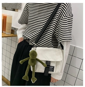 Detail of white canvas messenger bag with black buckle and green frog plush keychain