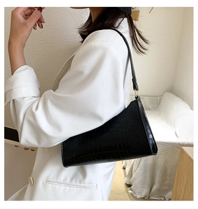 Side view of black faux leather baguette bag with crocodile texture on white blazer