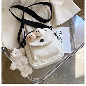 Detail of off-white canvas crossbody bag featuring 3D plush bears and black nylon strap