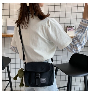 Detail of black canvas messenger bag with fashion label and green frog plush pendant