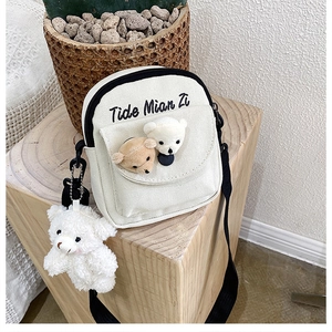 Detail of canvas crossbody bag with plush bear heads and a cute hanging charm