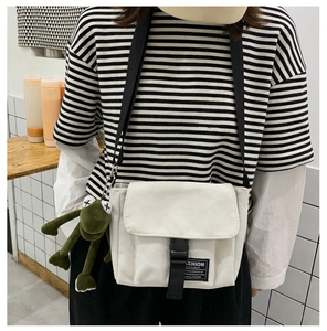 Detail of white canvas messenger bag with buckle strap and green frog plush toy