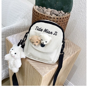 Detail of cream canvas crossbody bag with cute plush bear charms and black lettering