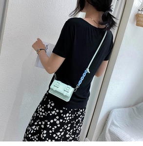 Detail van mintgroene mini crossbodytas met dubbele gespen en kettingriem op model