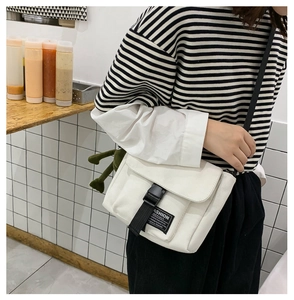 Detail of white canvas crossbody bag featuring black buckle and green frog plush charm