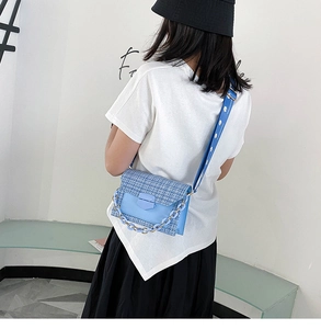 Detail of blue tweed crossbody bag with chain strap and wide shoulder strap on model
