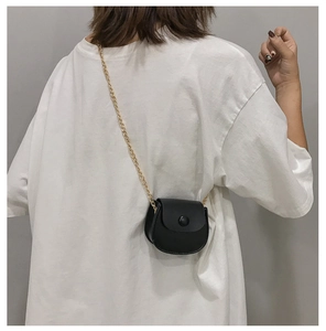 Detail van een zwarte mini zadeltas met matte afwerking en gouden ketting op model