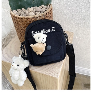 Detail of black canvas crossbody bag with cute bear patches and plush bear keychain charm