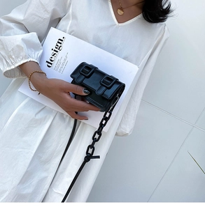 Detail van een zwarte mini crossbodytas met dubbele gespen en ketting op een witte jurk