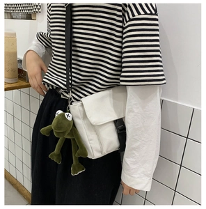 Detail of white canvas messenger bag with adjustable strap and plush green frog charm