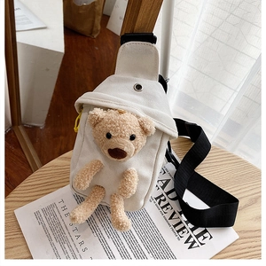 Close-up of a cream canvas chest bag featuring a 3D plush brown bear on a wooden desk