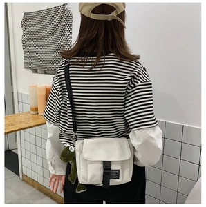 Detailed back view of white canvas crossbody bag with black buckle and dinosaur plush charm