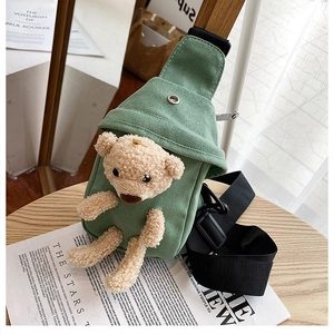 Detail of green canvas crossbody bag featuring a cute brown plush bear on wood table