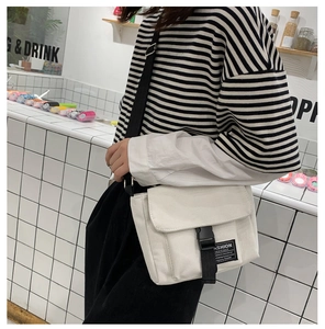 Detail of white canvas messenger bag featuring a black buckle closure and adjustable strap
