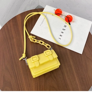 Bovenaanzicht van een gele mini leren crossbodytas met harsketting op een houten tafel