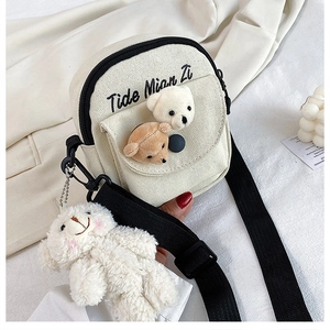 Detail of white canvas mini crossbody bag with plush bear charms and wide black strap