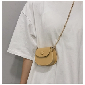 Detail van minimalistische beige zadeltas met fijne gouden ketting op een wit t-shirt