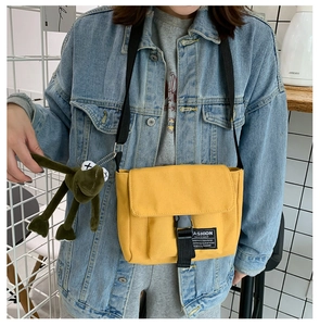 Detail of yellow canvas messenger bag with black buckle and green frog plush charm