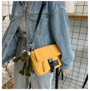 Detail of yellow canvas messenger bag with black buckle and green frog plush charm