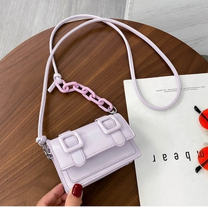 Detail van lavendelkleurige crossbodytas met dubbele gespen en plastic ketting op houten tafel