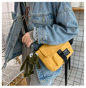 Detail of yellow canvas messenger bag with a green plush frog charm and buckle strap