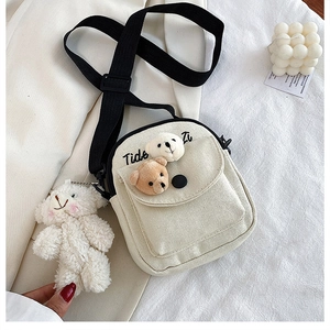 Detail view of the cream canvas bag with plush bear charms and a black strap