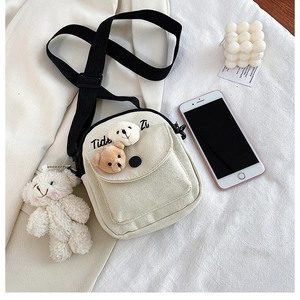 Close-up of cream canvas bag featuring plush bear charms and adjustable black strap