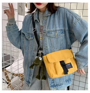 Yellow canvas messenger bag with adjustable strap and green frog plush charm on model