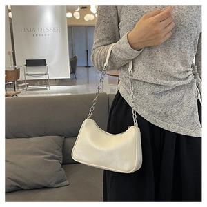 Chic white hobo bag with gold chain strap carried by model in a minimalist cafe setting