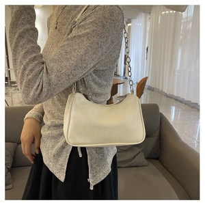 Detail view of cream leather underarm bag with metal chain strap on female model
