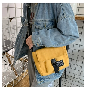 Detail of yellow canvas messenger bag featuring a black buckle and fashion woven label