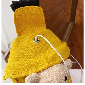 Detail of yellow canvas bag featuring a plush bear and metal grommet for cable exit