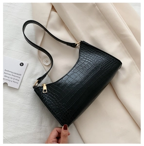 Detail view of black crocodile pattern baguette bag with golden zipper on fabric