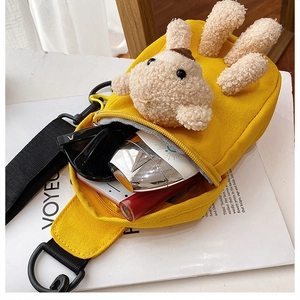 Detail of yellow canvas cross-body bag with 3D teddy bear decoration and daily essentials