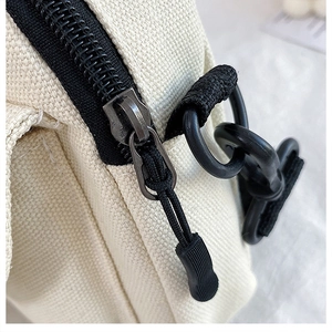 Close-up of off-white canvas bag featuring black metal zipper and D-ring hook details