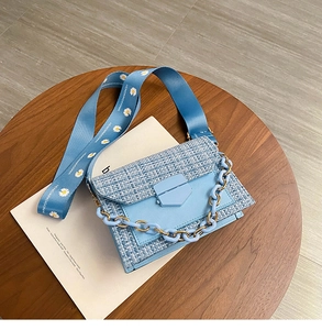 Detail of light blue tweed crossbody bag featuring daisy strap and chain link