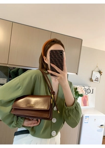 Close-up of brown textured leather crossbody bag with elegant gold brand logo detailing