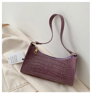 Detail of purple crocodile-patterned underarm bag with gold zipper and leather texture