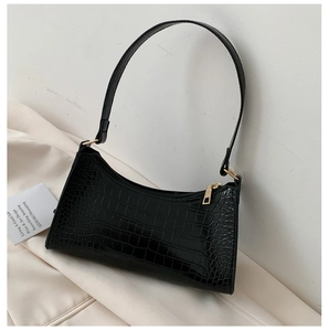 Detail of black crocodile texture on baguette bag with golden metal zipper and hardware