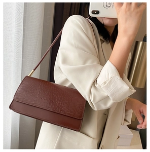 Detail of a brown crocodile pattern shoulder bag with elegant gold metal hardware on model